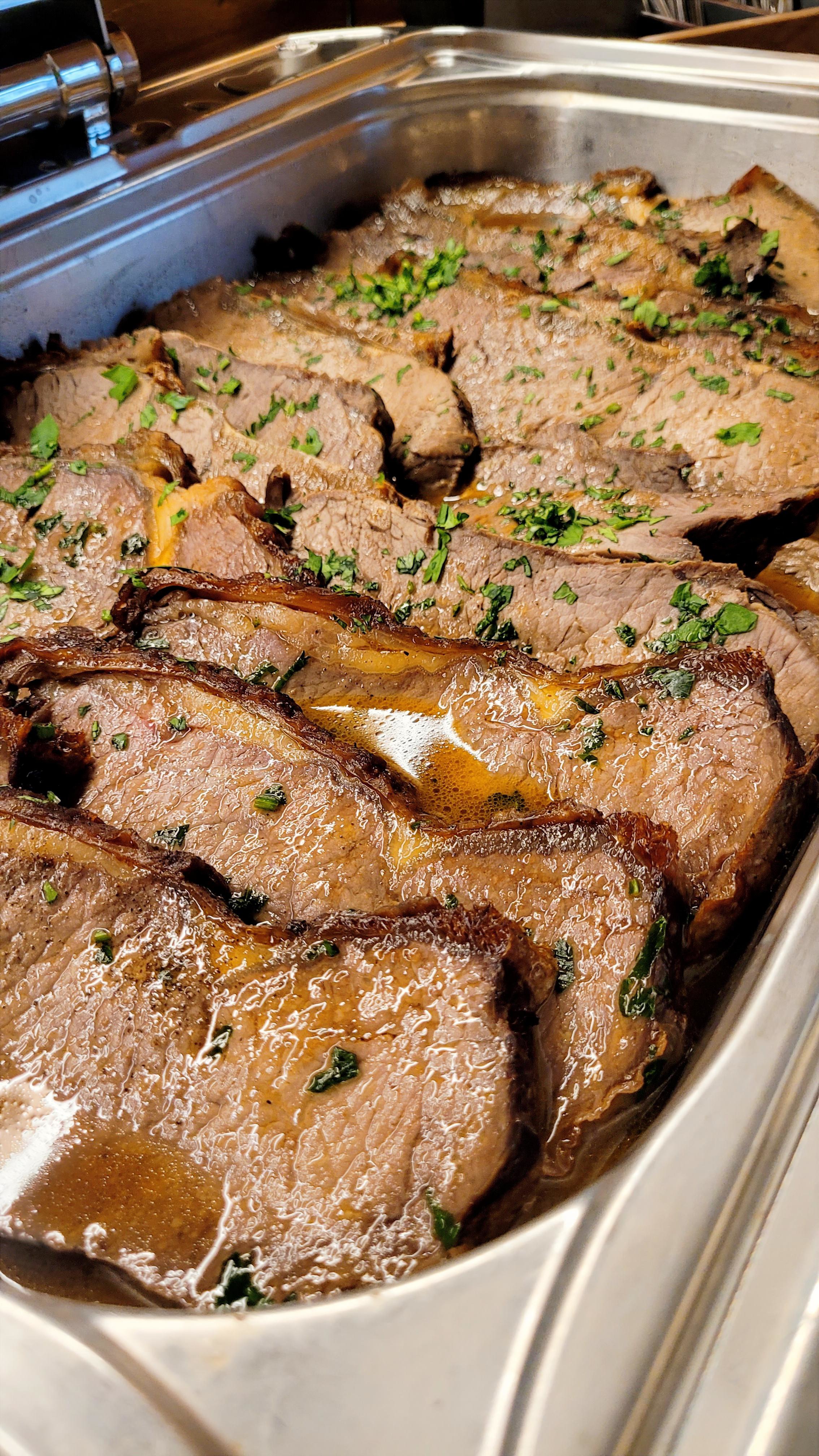 Mehrere saftige Rinderbratenscheiben liegen in Soße und sind mit Kräutern bestreut