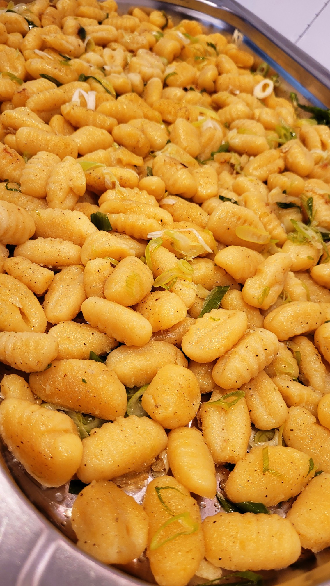 Ein Blech voller goldbrauner Gnocchi mit frischen grünen Kräutern und Zwiebeln